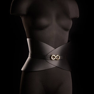 Corset ceinture HUDIA IINFYNII en cuir noir avec fermoir métallique infini porté sur un tailleur noir, accessoire structurant et graphique proposé par Brigade Mondaine Paris