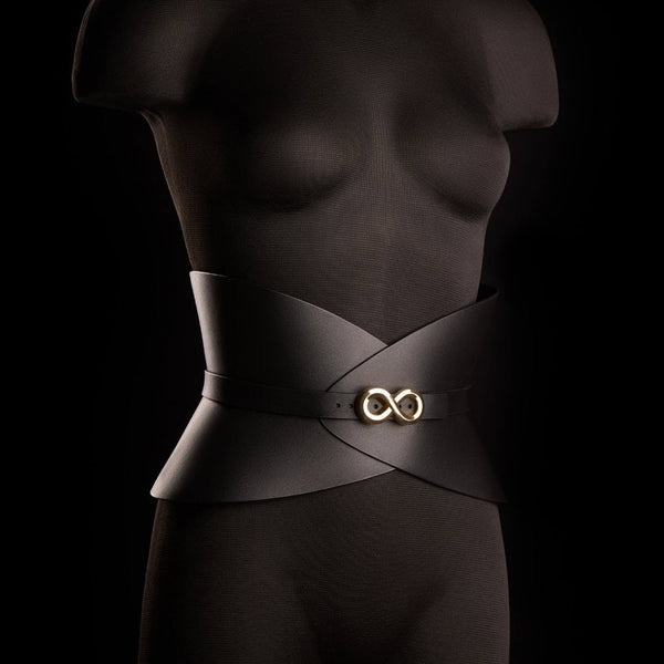 Corset ceinture HUDIA IINFYNII en cuir noir avec fermoir métallique infini porté sur un tailleur noir, accessoire structurant et graphique proposé par Brigade Mondaine Paris