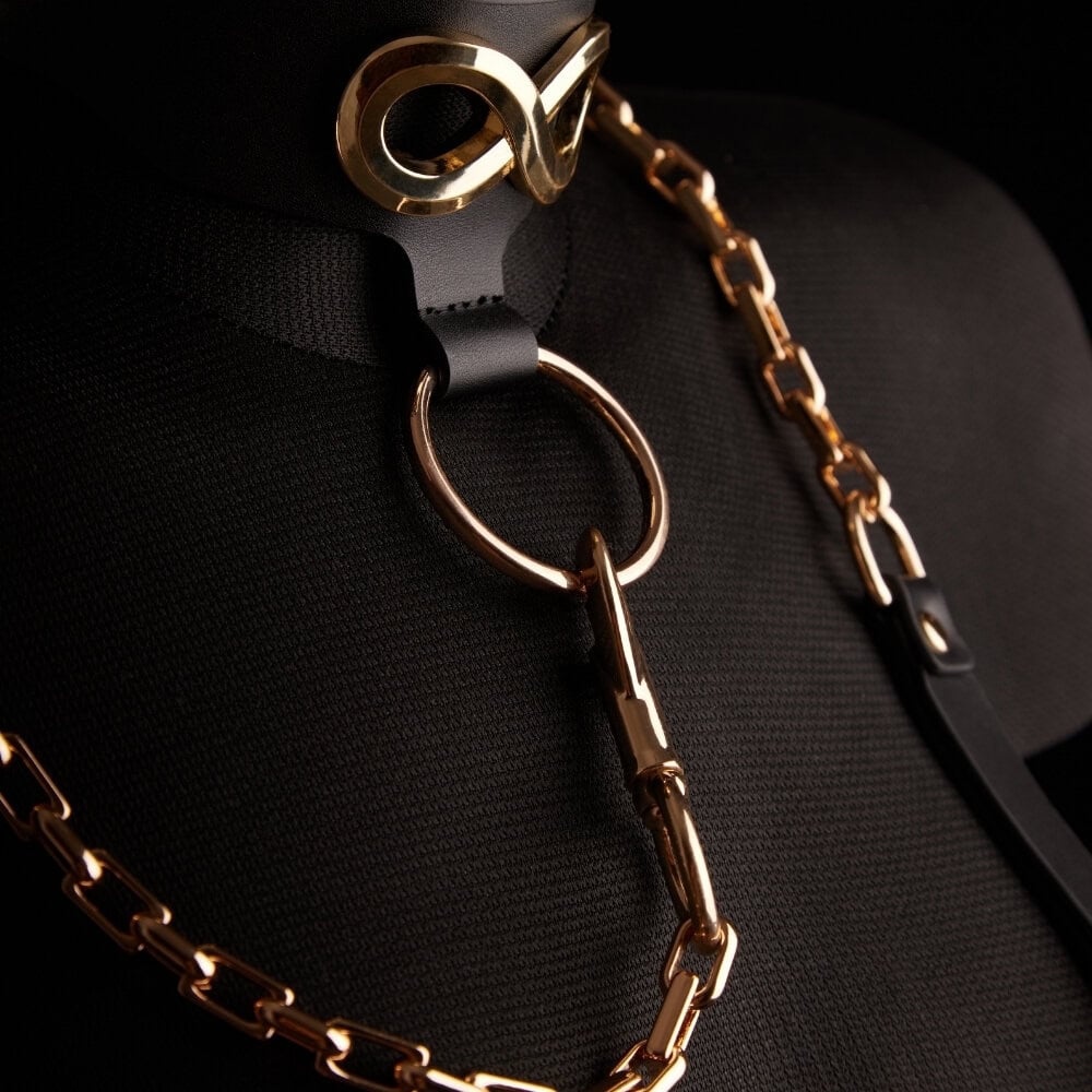 Le collier laisse SEVERA de IINFYNII associe cuir noir et chaîne métallique dorée dans une construction affirmée et structurante. Pensé comme une pièce de corps forte, il se compose d’un collier en cuir orné d’un symbole métallique signature, prolongé par une chaîne articulée reliée à un anneau central. Ajustable, il peut se porter seul ou intégré à une silhouette complète, entre bijou de contrainte et accessoire sculptural. Une pièce graphique, directe, conçue pour celles et ceux qui envisagent le corps co