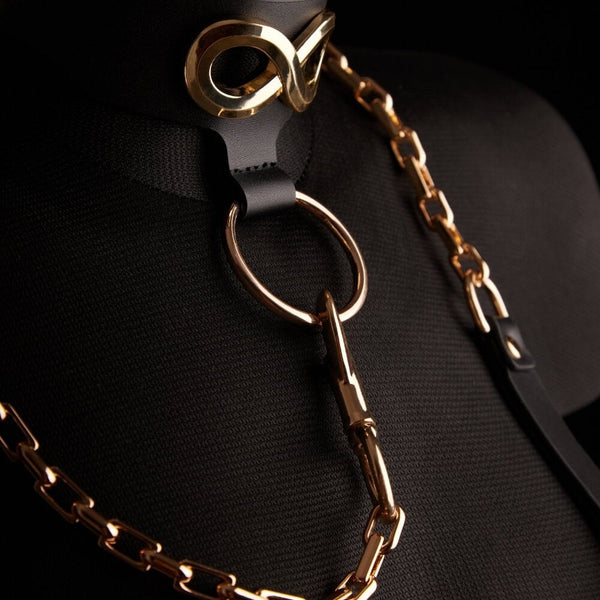 Le collier laisse SEVERA de IINFYNII associe cuir noir et chaîne métallique dorée dans une construction affirmée et structurante. Pensé comme une pièce de corps forte, il se compose d’un collier en cuir orné d’un symbole métallique signature, prolongé par une chaîne articulée reliée à un anneau central. Ajustable, il peut se porter seul ou intégré à une silhouette complète, entre bijou de contrainte et accessoire sculptural. Une pièce graphique, directe, conçue pour celles et ceux qui envisagent le corps co