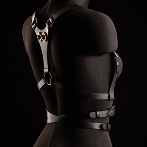 Harnais TRISCA IINFYNII en sangles noires avec boucles dorées et détail central, accessoire structurant porté sur le buste proposé par Brigade Mondaine Paris