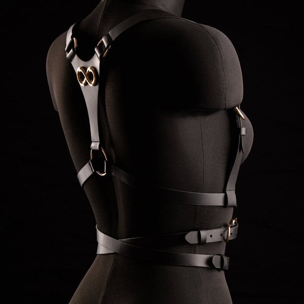 Harnais TRISCA IINFYNII en sangles noires avec boucles dorées et détail central, accessoire structurant porté sur le buste proposé par Brigade Mondaine Paris
