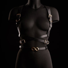 Harnais TRISCA IINFYNII en sangles noires avec boucles dorées et détail central, accessoire structurant porté sur le buste proposé par Brigade Mondaine Paris