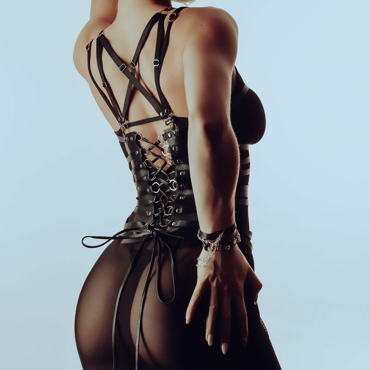 Harnais en satin élastique et cuir noir, ajustable, avec fermeture corsetée. Design graphique et sensuel, structurant la silhouette. Pièce audacieuse et polyvalente.