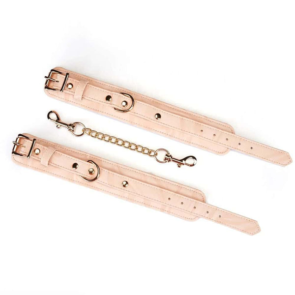 Menottes Boudoir Amor en similicuir vegan rose pastel et noir. Finitions dorées, anneau en D pour fixation. Boucles ajustables et clips à dégagement rapide pour sécurité et confort. Idéales pour des jeux de soumission élégants.