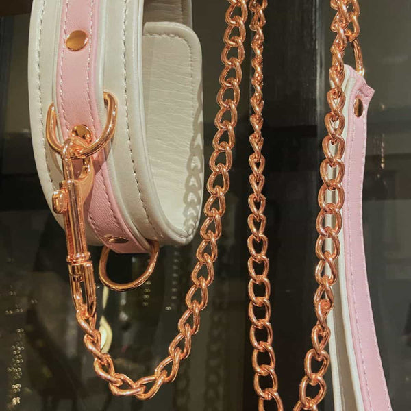 Collier BDSM FAIRY en cuir blanc et rose pastel avec laisse assortie en or rose. Confortable, ajustable et raffiné, cet accessoire bondage haut de gamme est disponible chez Brigade Mondaine.