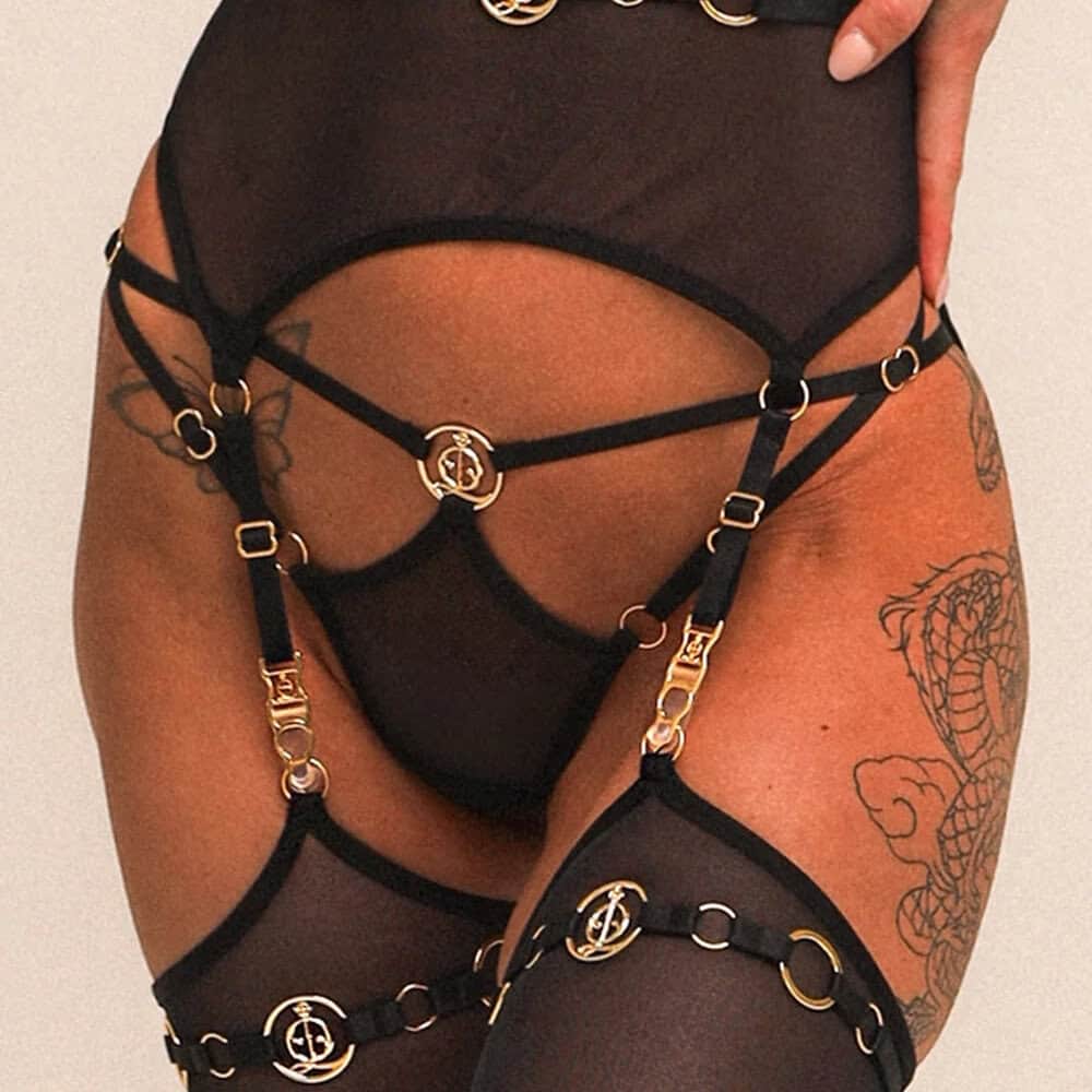Body QRUCIFIX en mesh noir avec découpes au buste, harnais intégré et jambières assorties, porté par un modèle sur fond clair, présenté par Brigade Mondaine Paris.