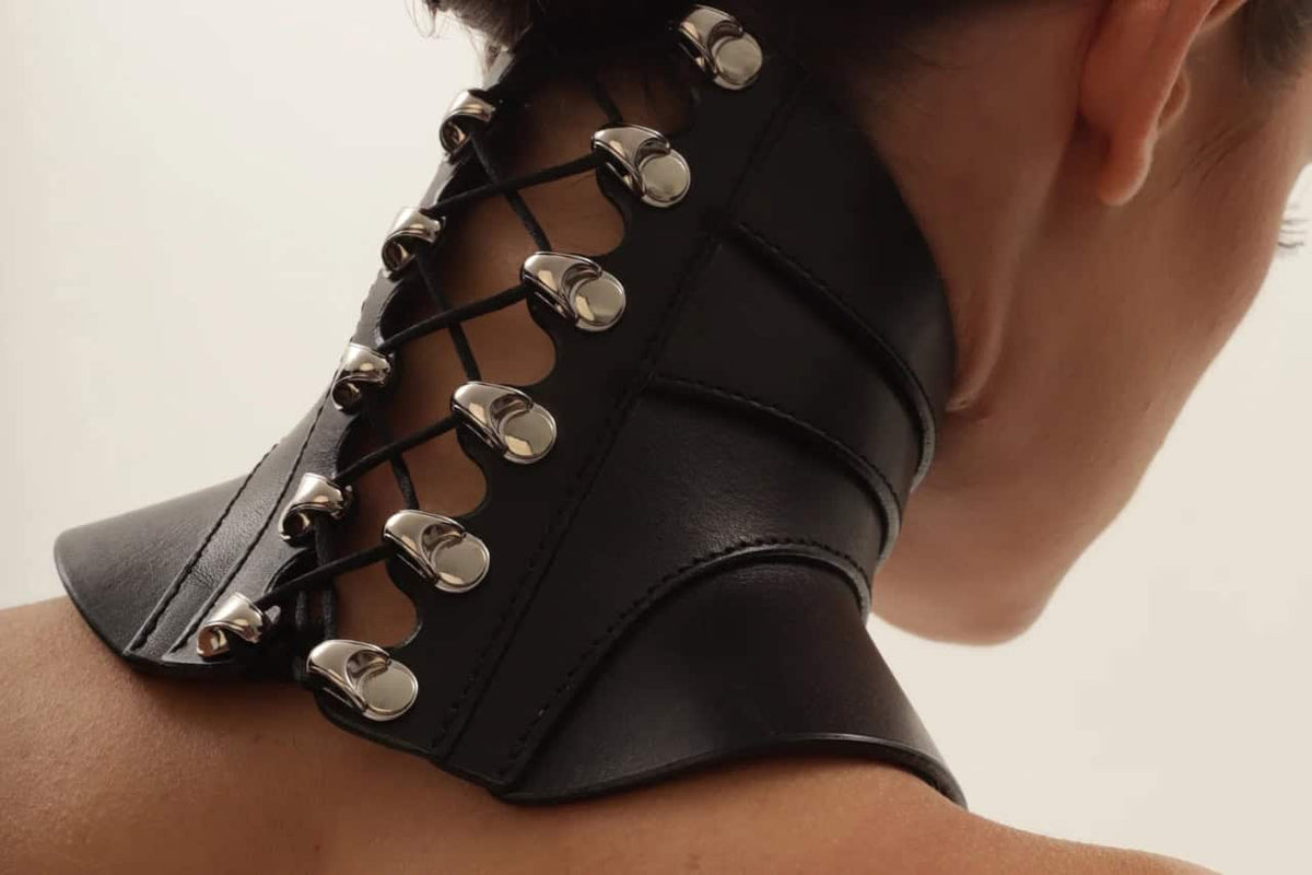 Collier posture TENUE RE:STRICT en cuir noir avec laçage et éléments métalliques, porté au cou, sélection Brigade Mondaine Paris.