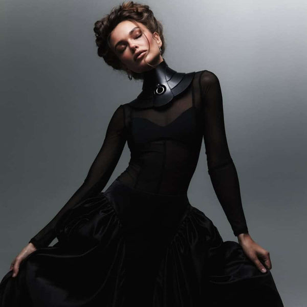 Mannequin portant le collier Posture Hold en cuir noir RE:STRICT chez Brigade Mondaine Paris, pièce rigide couvrant le cou, anneau métallique central, porté avec un top en mesh noir en studio.