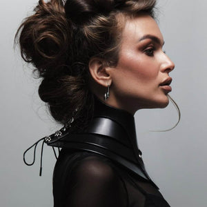 Mannequin portant le collier Posture Hold en cuir noir RE:STRICT chez Brigade Mondaine Paris, pièce rigide couvrant le cou, anneau métallique central, porté avec un top en mesh noir en studio.