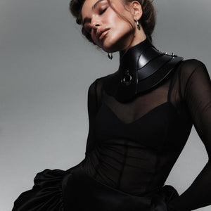Mannequin portant le collier Posture Hold en cuir noir RE:STRICT chez Brigade Mondaine Paris, pièce rigide couvrant le cou, anneau métallique central, porté avec un top en mesh noir en studio.