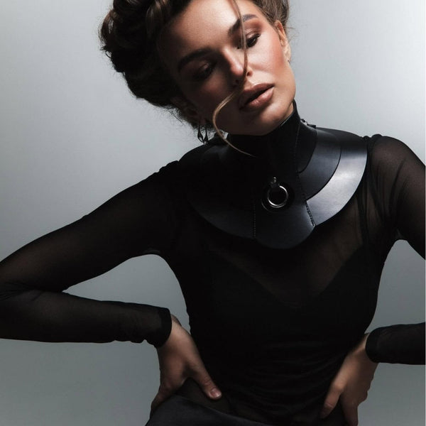 Mannequin portant le collier Posture Hold en cuir noir RE:STRICT chez Brigade Mondaine Paris, pièce rigide couvrant le cou, anneau métallique central, porté avec un top en mesh noir en studio.
