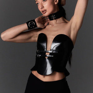 Mannequin portant le corset Daelos en cuir noir RE:STRICT chez Brigade Mondaine Paris, décolleté plongeant structuré, sangles ajustables, porté avec accessoires assortis sur fond rouge.