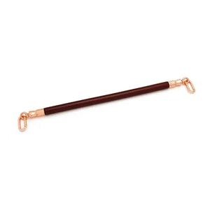 Barre d’écartement en cuir rouge vin avec noyau en bois d’eucalyptus. Joints toriques en métal or rose pour fixer des chevillières. Élégante et fonctionnelle pour des jeux BDSM raffinés.