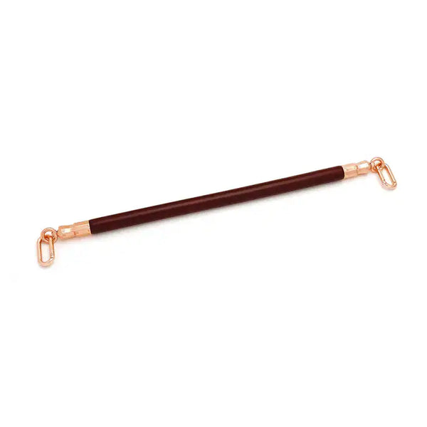 Barre d’écartement en cuir rouge vin avec noyau en bois d’eucalyptus. Joints toriques en métal or rose pour fixer des chevillières. Élégante et fonctionnelle pour des jeux BDSM raffinés.