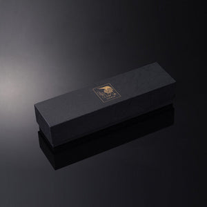 Le packaging UPKO, noir et doré, est disposé en diagonale sur un fond noir brillant qui capte et reflète la lumière blanche.