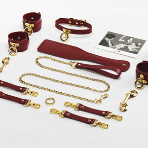 Accessoires de cuir bordeaux rouge BDSM et détails en or 24K, menottes de poignets, chevilles et cuisses et collier et laisse, paddle pour fessée UPKO chez Brigade Mondaine