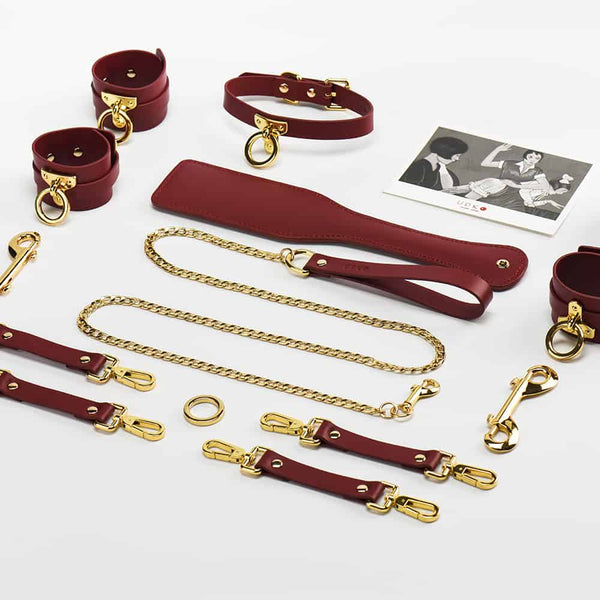 Accessoires de cuir bordeaux rouge BDSM et détails en or 24K, menottes de poignets, chevilles et cuisses et collier et laisse, paddle pour fessée UPKO chez Brigade Mondaine