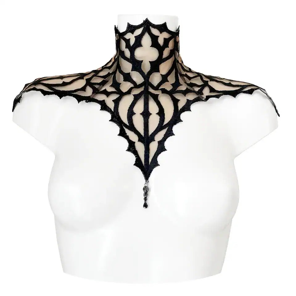 Plastron gothique brodé noir sur tulle nude, orné d’un pendentif central. Forme montante couvrant cou et épaules. Fermeture réglable par ruban façon corset au dos.