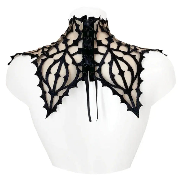 Plastron gothique brodé noir sur tulle nude, orné d’un pendentif central. Forme montante couvrant cou et épaules. Fermeture réglable par ruban façon corset au dos.