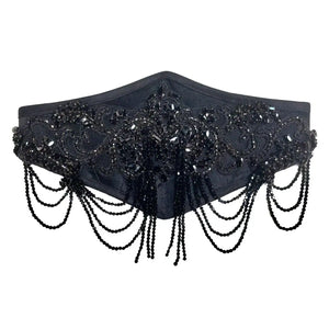Handmade black velvet waist belt featuring an intricate hand-applied glass-beaded appliqué and cascading rows of faceted black glass beads. Designed to combine structure and fluid movement, this belt is crafted on a soft velvet base and finished with an adjustable velvet elastic band for comfort, flexibility, and a secure fit on the waist or hips. Each piece is meticulously crafted upon order, making every creation unique. For this reason, bead placements and appliqué details may vary slightly from those pi