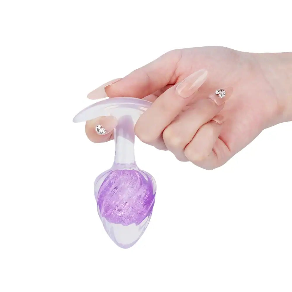 Plug en silicone violet LIEBE SEELE avec surface spiralée et base transparente évasée, tenu en main sur fond blanc, vue produit détaillée