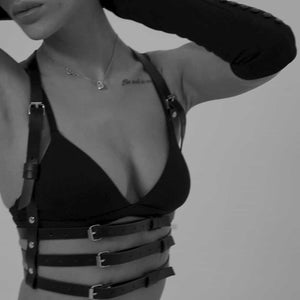 Femme en noir et blanc portant un harnais en cuir naturel fait à la main, avec trois lanières sous le buste et deux lanières montant vers le cou, créant un effet de soutien-gorge. Elle porte également un soutien-gorge noir, et le cuir est mis en valeur par la lumière, accentuant la texture et le design sophistiqué.