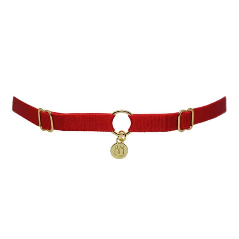 Aquí puede ver el BRIGADE MONDAINE GIFT WRAP RED. Este collar está hecho de una banda roja. Hay 2 detalles para ajustar las bandas a la derecha y a la izquierda. En el centro, la banda está separada por un anillo chapado en oro con un colgante que dice "BM".