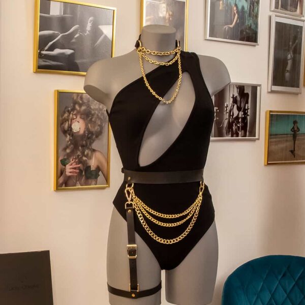 We can see a model wearing the Nadine bodysuit from Ow Intimates, it is black and has a slit going from the neck to under the chest diagonally. He is also wearing an Elif Domanic bondage chocker in gold color. And a leather garter belt from Mia Atelier in black and gold.