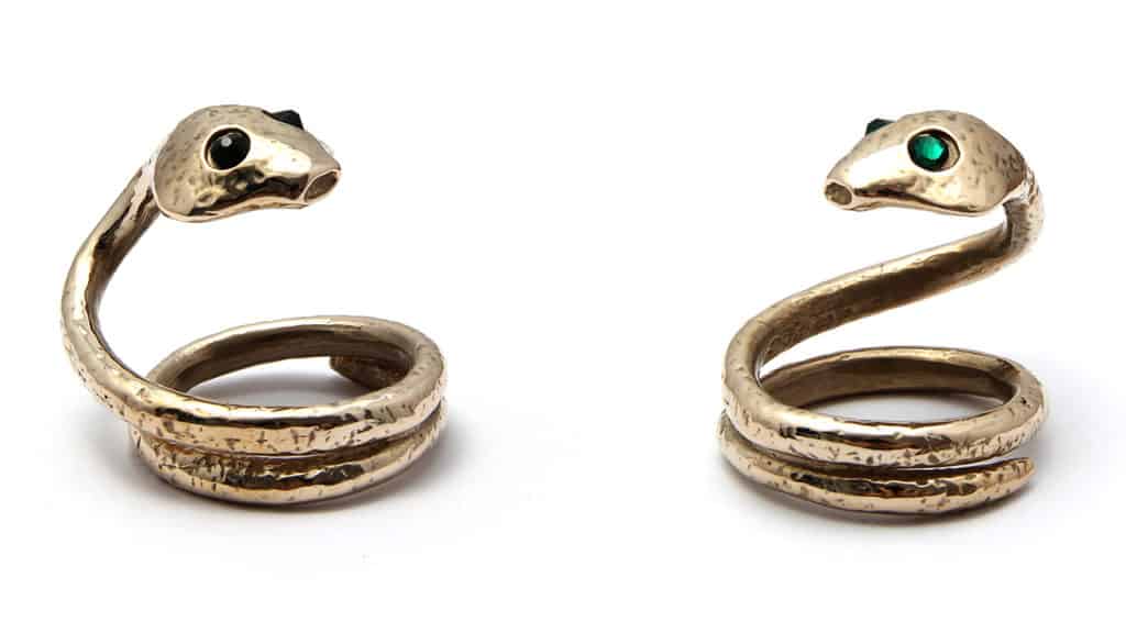 Esta foto muestra dos anillos con forma de serpiente. Uno tiene piedras negras como ojos y el otro, esmeraldas. La cola de la serpiente se enrosca para formar un anillo ancho.