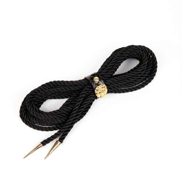 Le Leone Lasso Shibari de Fraulein Kink. Les lassos de bondage ont de nombreuses options polyvalentes pour une utilisation à l'intérieur ou à l'extérieur de la chambre. Portez-le comme une ceinture ou un harnais pour ajouter une touche haute couture à votre tenue préférée. 5 mètres de corde noire. Embouts à tête de lion or. Sécurisé avec un bracelet en cuir gaufré croco avec bouton doré.