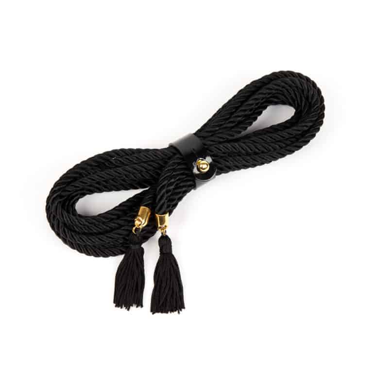 Le Ricco Lasso de Fraulein Kink. Les lassos de bondage ont de nombreuses options polyvalentes pour une utilisation à l'intérieur ou à l'extérieur de la chambre. Portez-le comme une ceinture ou un harnais pour ajouter une touche haute couture à votre tenue préférée. 5 mètres de corde noire. Embouts à pampilles plaqués or. Sécurisé avec un bracelet en cuir verni avec bouton doré.