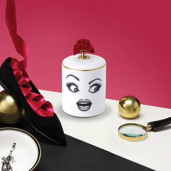 Kerze Muse Parfumée Ein überraschtes Gesicht, zart mit Filz auf weißes Porzellan mit goldenen und roten Details gezeichnet, auf einem weißen Tisch an einer rosa Wand, auf der eine Ballerina mit einer Schleife thront.