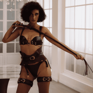 Photograph of a woman wearing a brown lingerie ensemble and holding a whip in front of her.