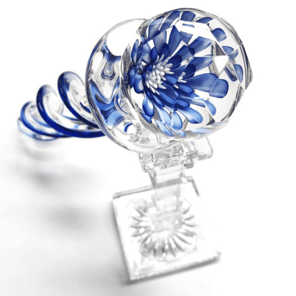 Fotografía sobre fondo blanco, packshot, consolador de cristal sobre trípode, transparente con forma de espiral y pintura azul y blanca en su interior.