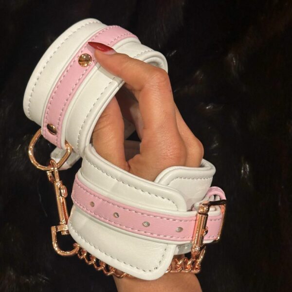 Bild der Handschellen aus weißem und rosafarbenem Leder, die auf einem schwarzen Pelzhintergrund getragen werden