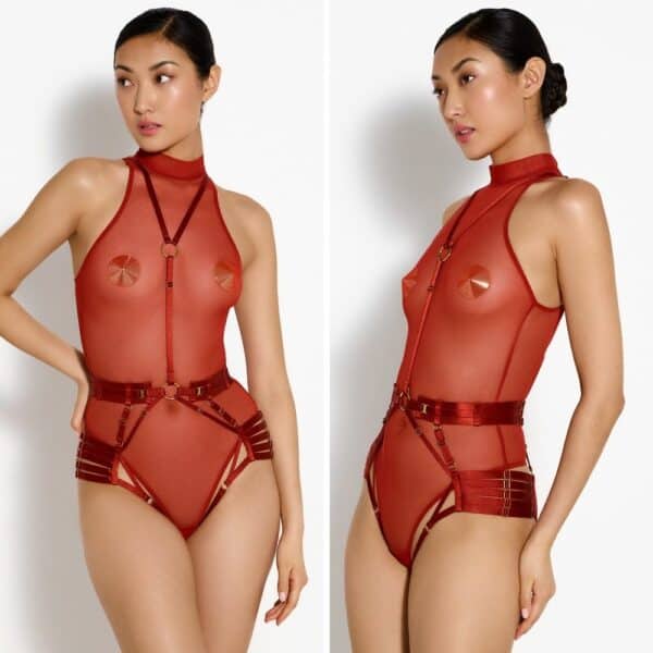 Foto einer Frau von vorne und von 3/4, die einen zweiteiligen Body Harness und einen roten Netzbody mit goldenen Nippies trägt.