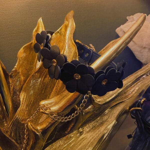 Collier et laisse en cuir noir avec design fleurs et chaine en or, posés sur une décoration dorée