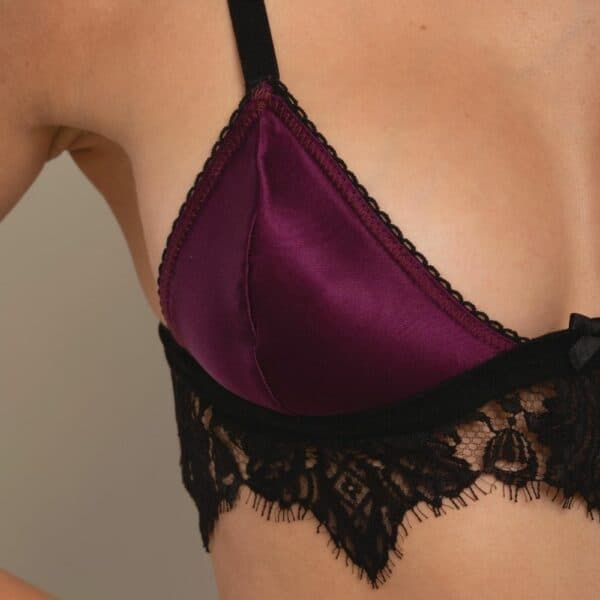 BH-Detail einer Frontfrau, die einen Triangel-Bralette-BH, einen Strapsgürtel und ein offenes Höschen aus violettem Satin und schwarzer Spitze trägt.